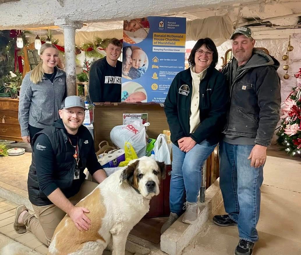 Group of people and a dog by a donation box; indoor setting, Christmas decorations.