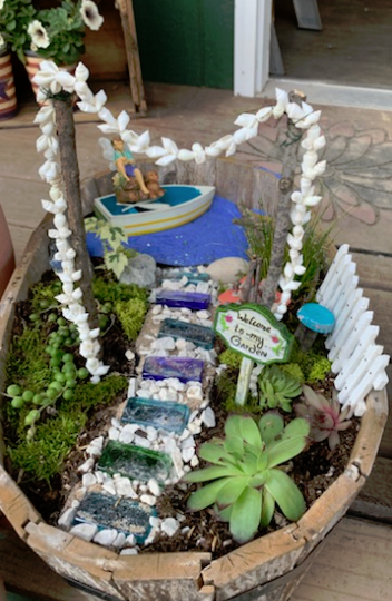 Miniature fairy garden in a wooden bowl with a stone path and a tiny boat.