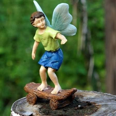 Fairy figurine skateboarding on a wooden platform; green shirt, blue shorts, teal wings.