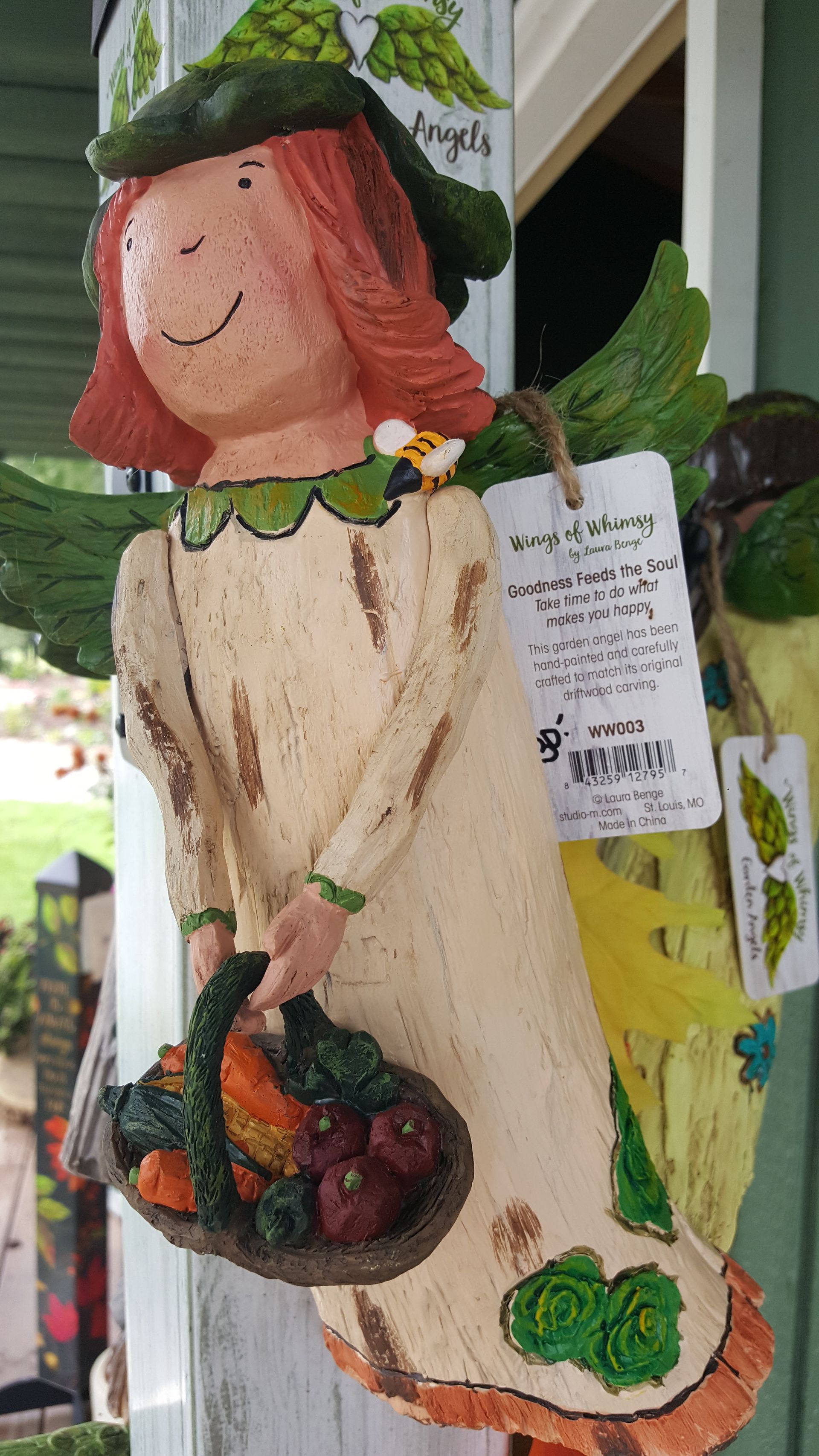Angel figurine holding basket of produce, wearing green hat, cream dress, and freckles.