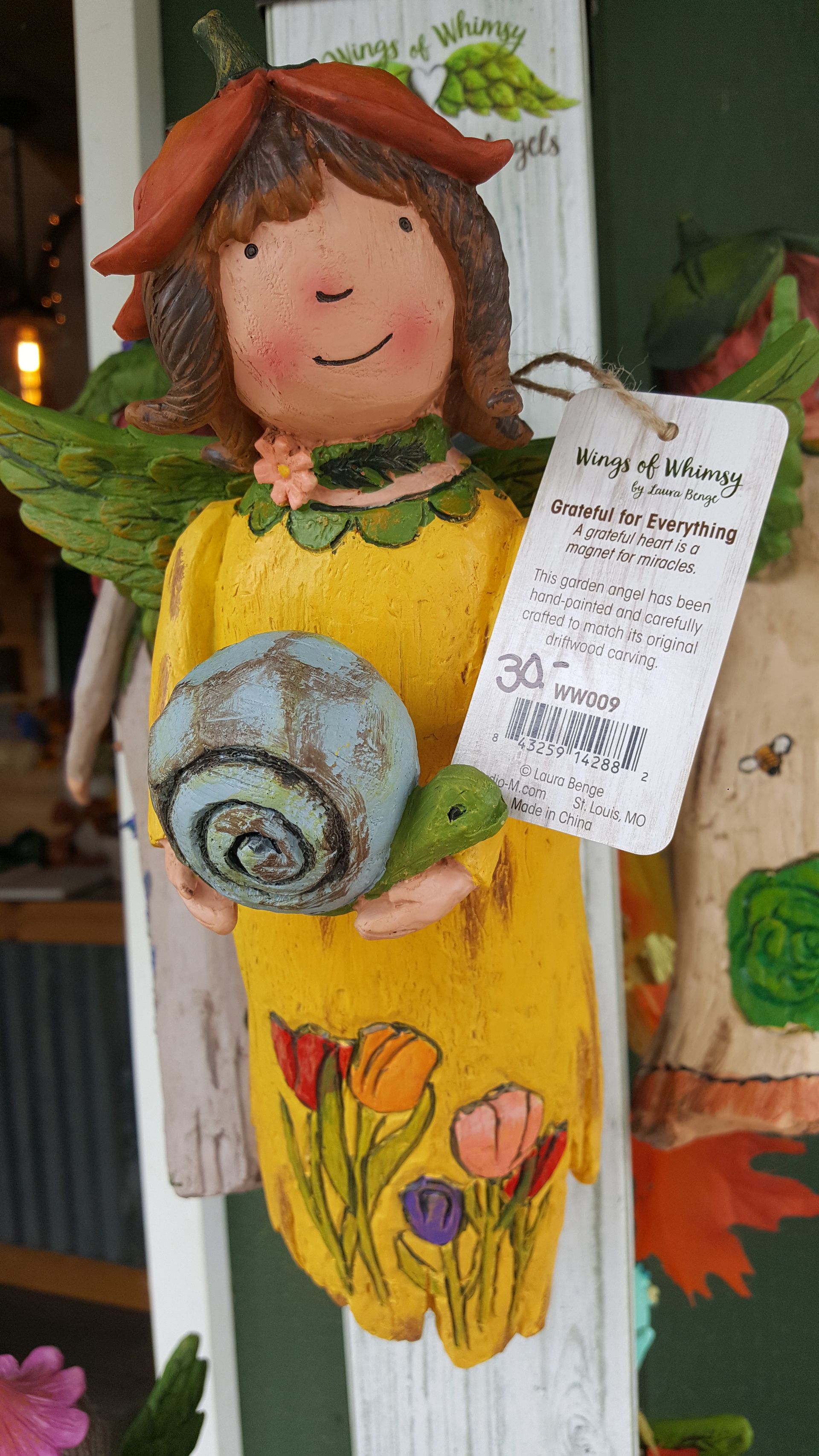Yellow fairy figurine holding a blue snail, wearing a flower hat, and a tag.