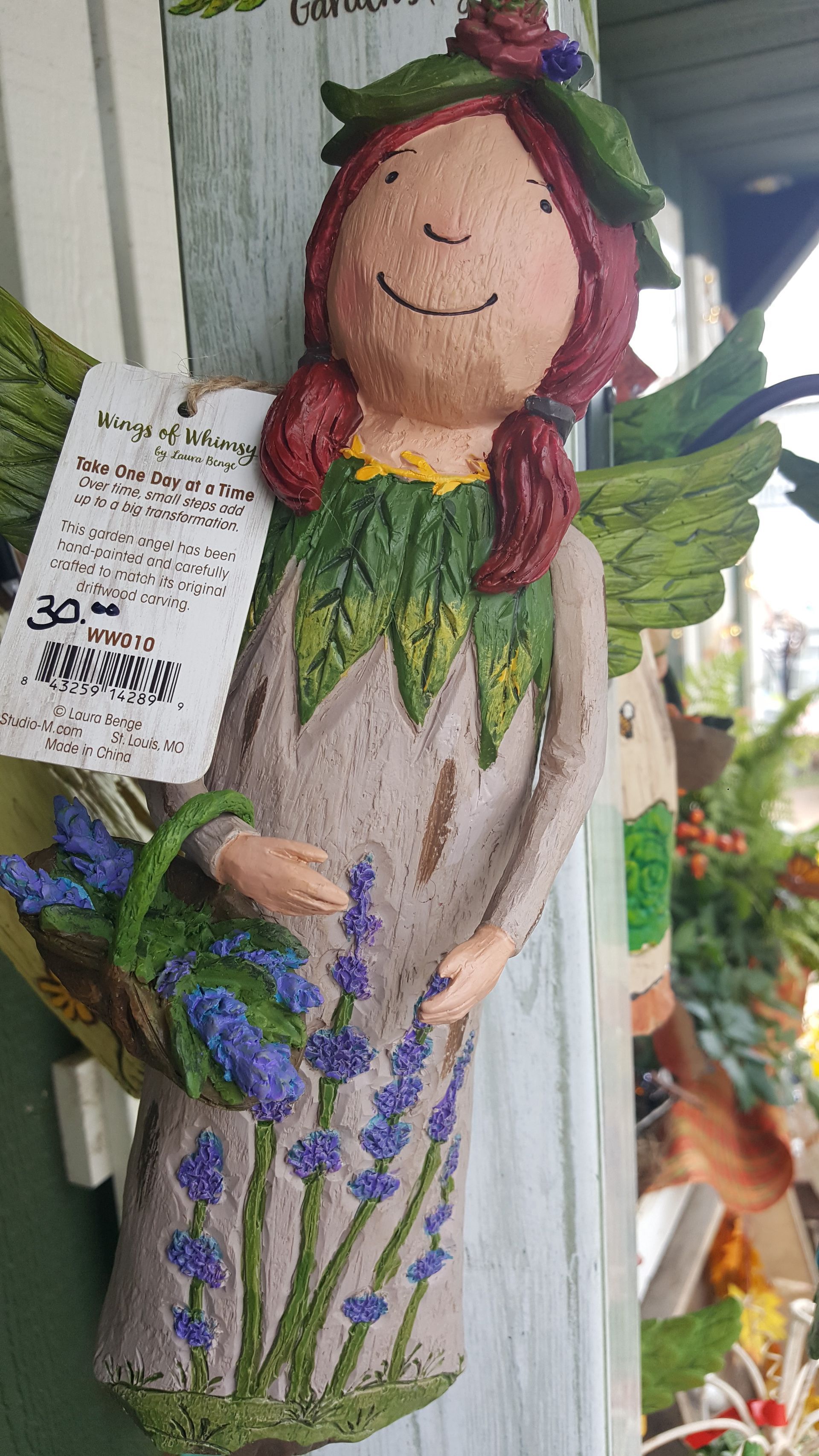 Fairy figurine holding a basket of lavender. Green wings, reddish-brown hair, and lavender dress.