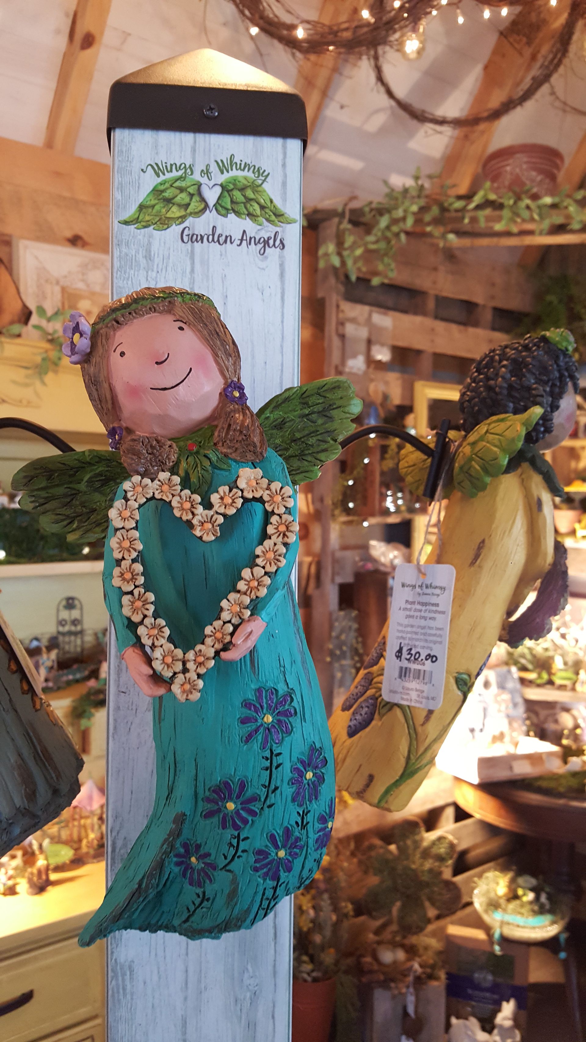Angel figurine holding floral heart, teal dress, displayed in a store.