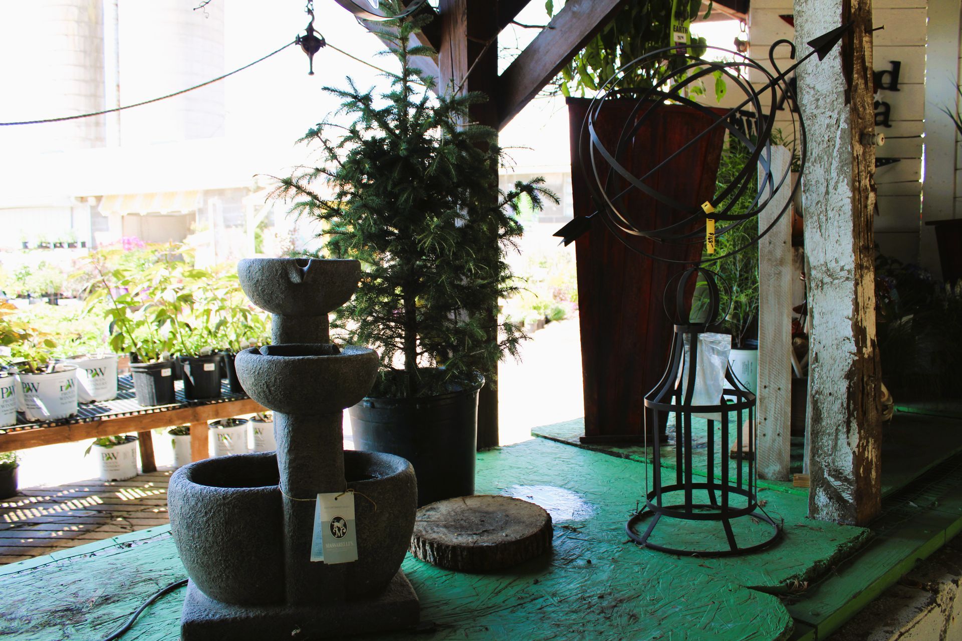 A water fountain on a green-painted counter with plants and a wooden slice in an outdoor setting.