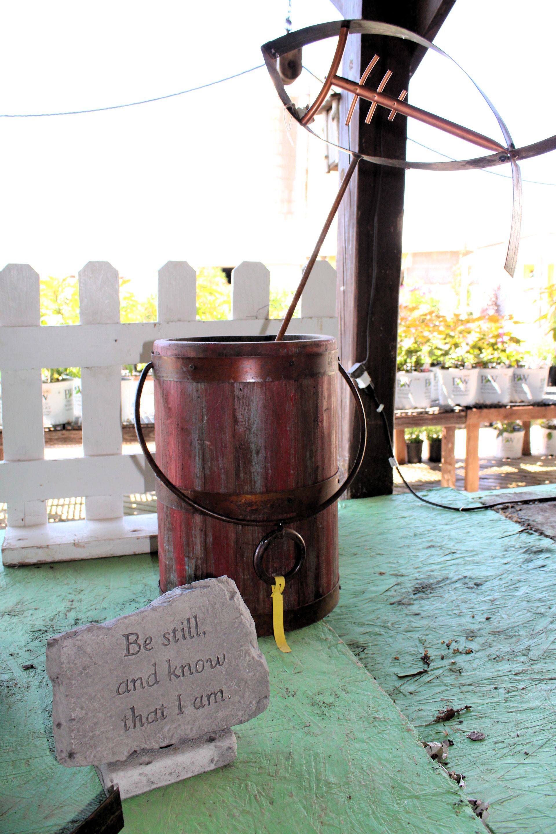 A weathered wooden bucket with a hanging handle, next to a sign that says 
