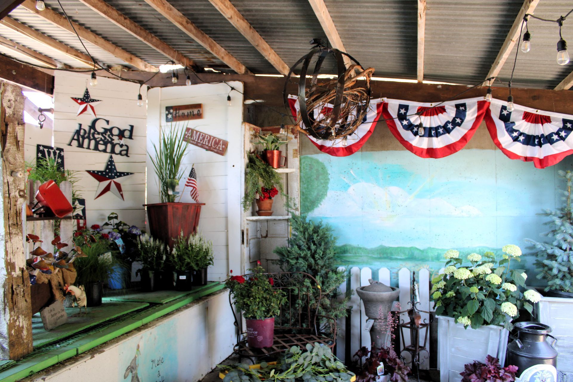 Rustic, decorated outdoor area with patriotic bunting, stars, and potted plants. A mural of a sky backdrop is visible.