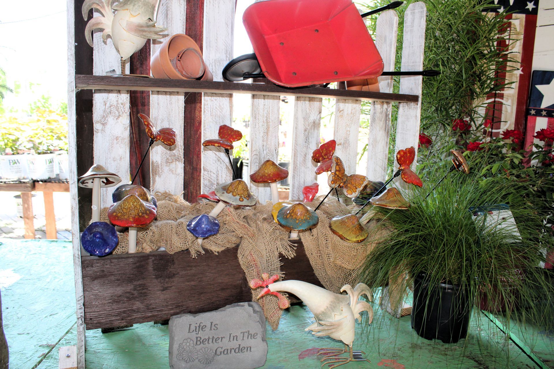 Garden display with mushroom decor, rooster, red wheelbarrow, and painted wooden fence.