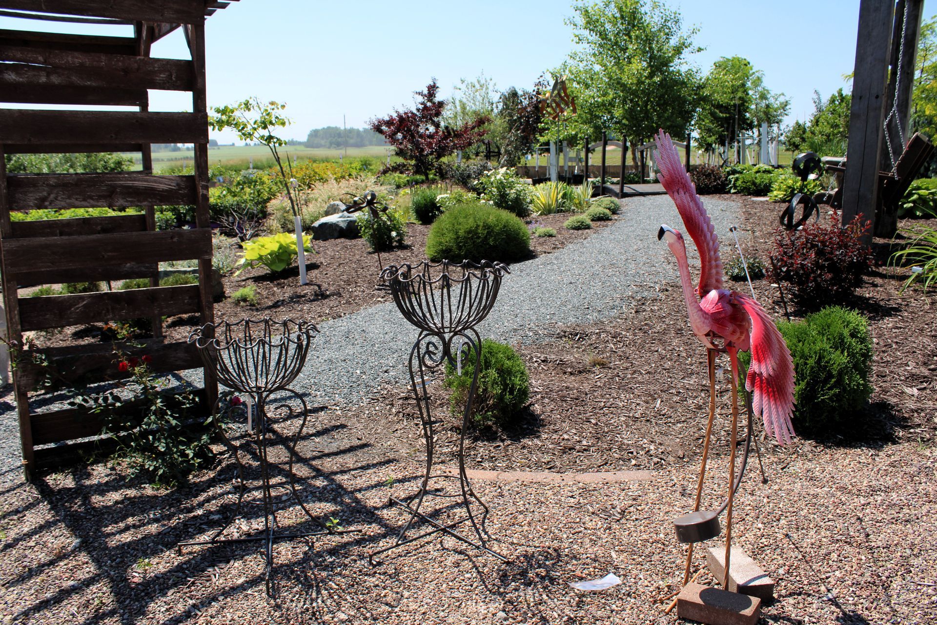 Garden scene with gravel paths, decorative metal figures, and greenery.