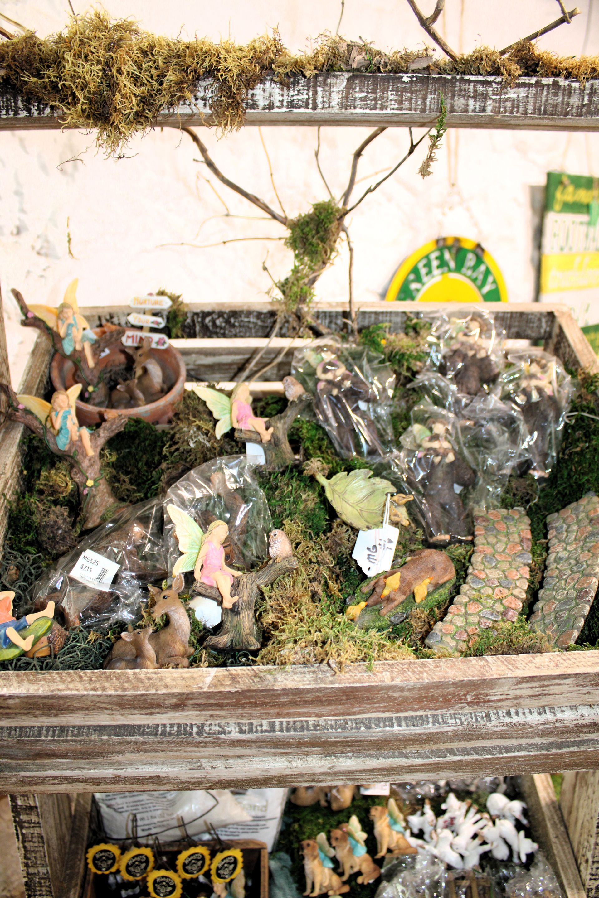 Display case with fairy garden items: figurines, moss, and decorative stones.
