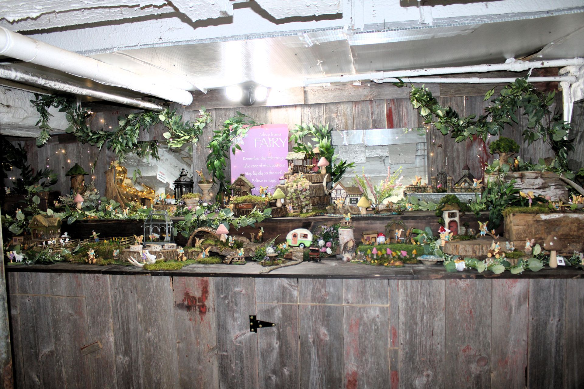 A whimsical display with miniature figurines and greenery set on a wooden shelf in an indoor space.