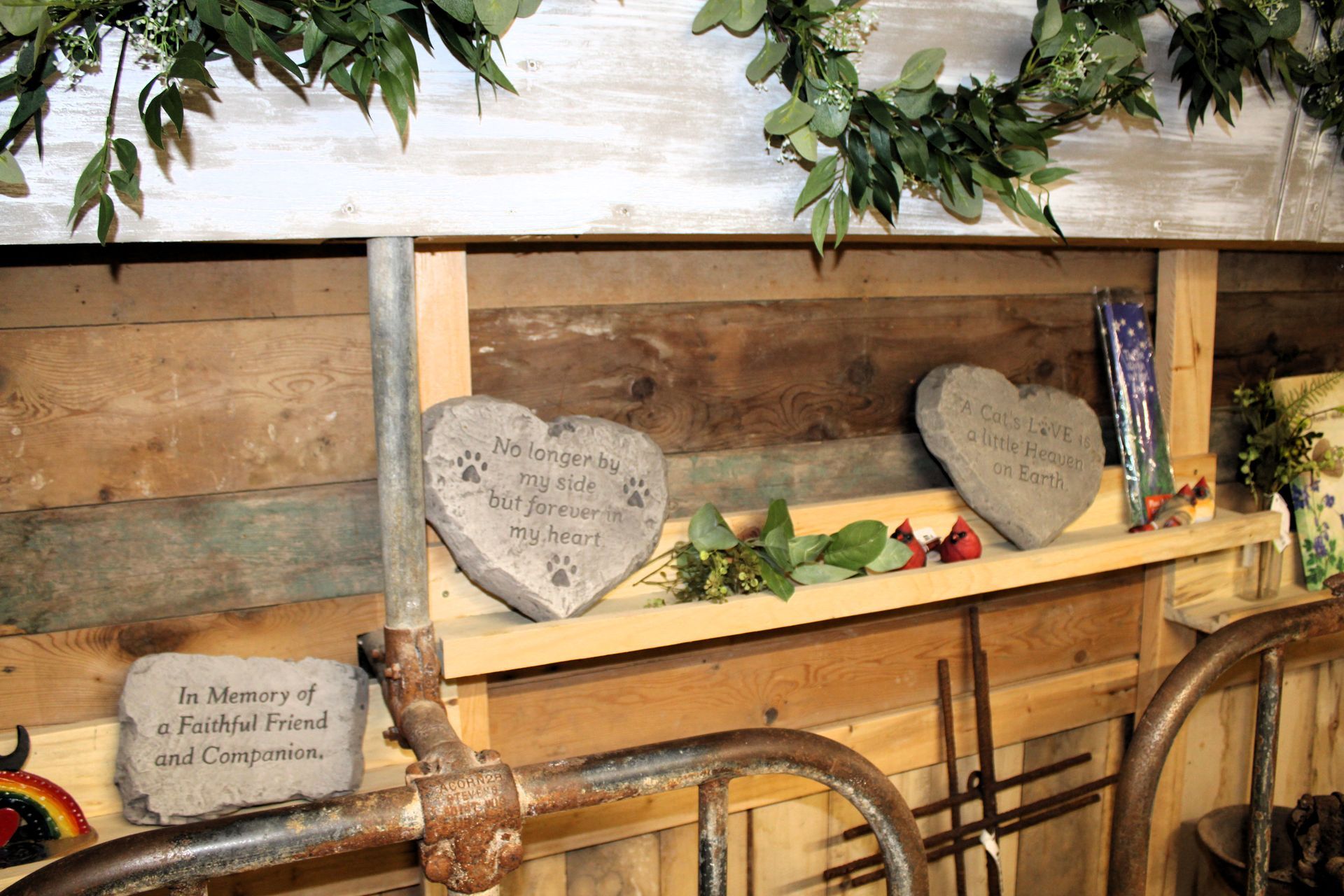 Heart-shaped memorial stones on a wooden shelf, with floral accents and greenery.