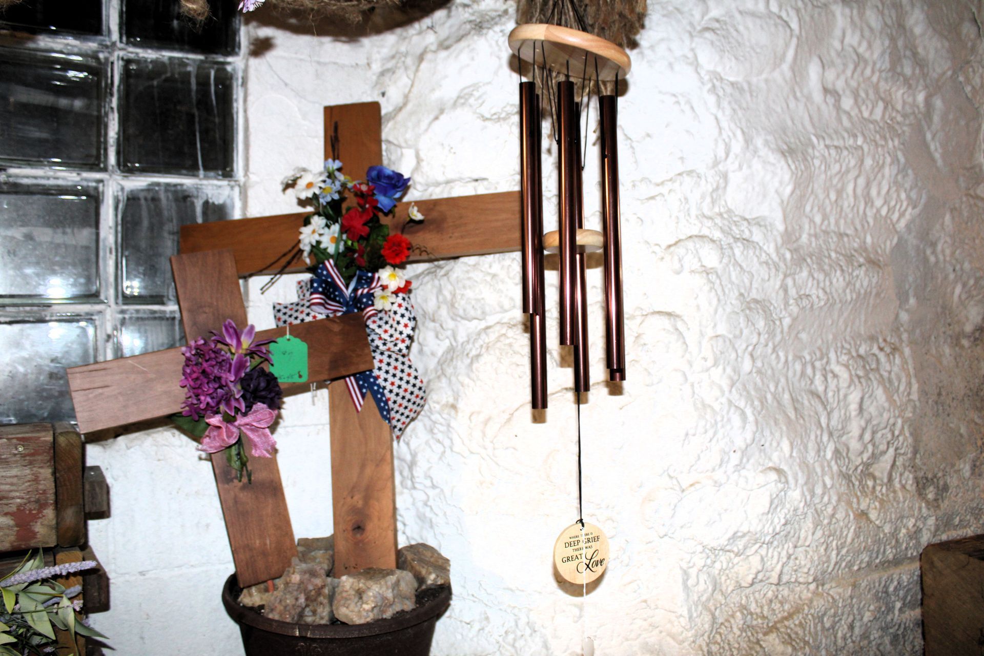 Two wooden crosses decorated with flowers and a wind chime in front of a textured wall.