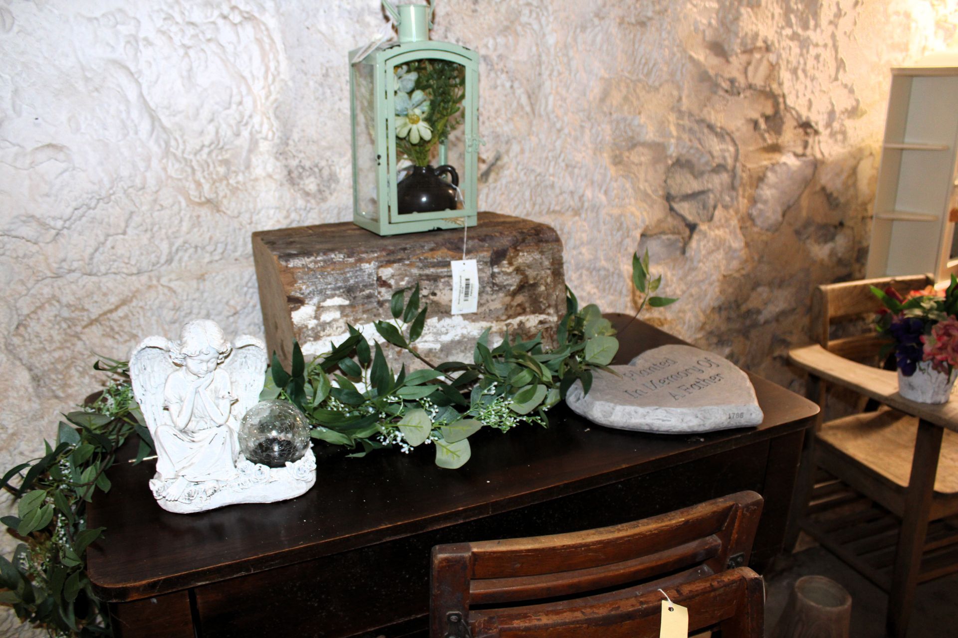 A display with an angel statue, lantern, and stone items on a dark wooden table in a room with stone walls.