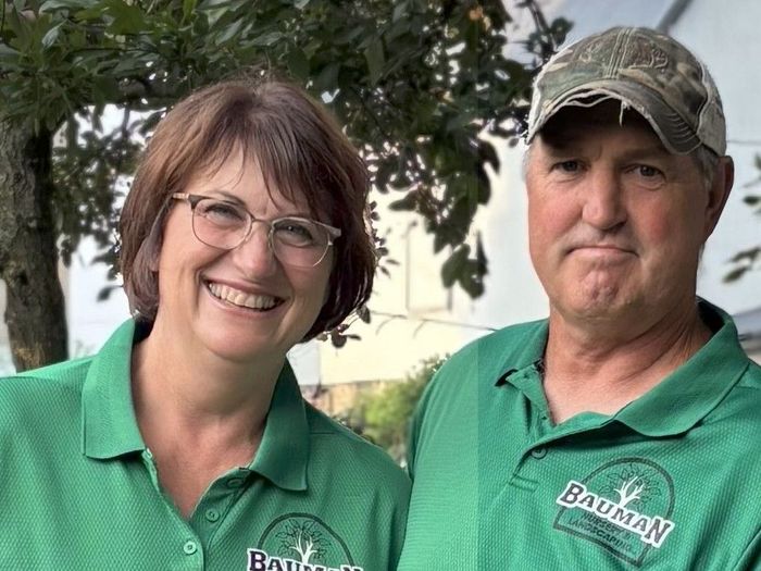 A woman in a denim jacket is smiling in front of a wooden wall