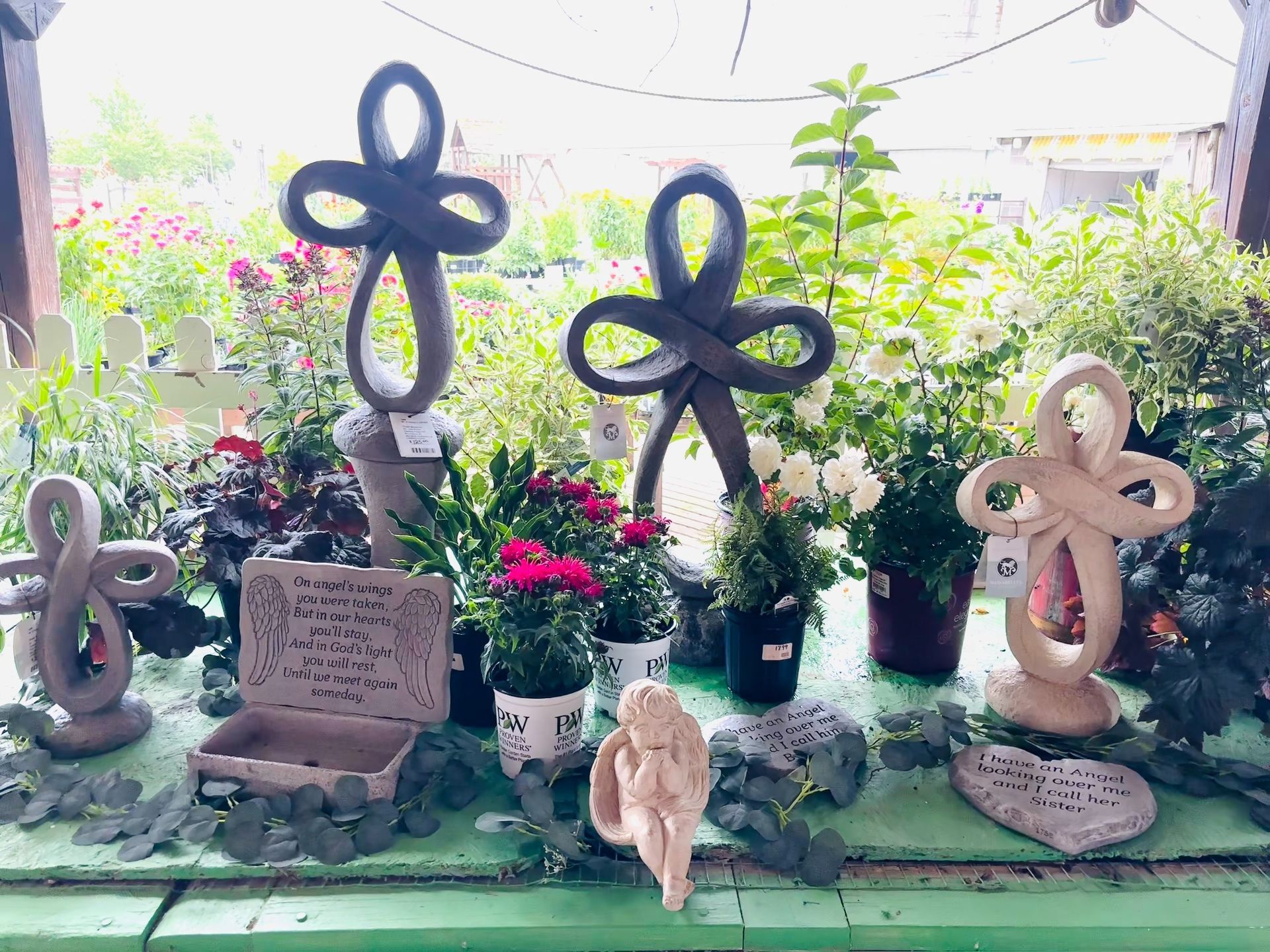 Display of garden ornaments, including loop sculptures, with potted flowers in a greenhouse setting.