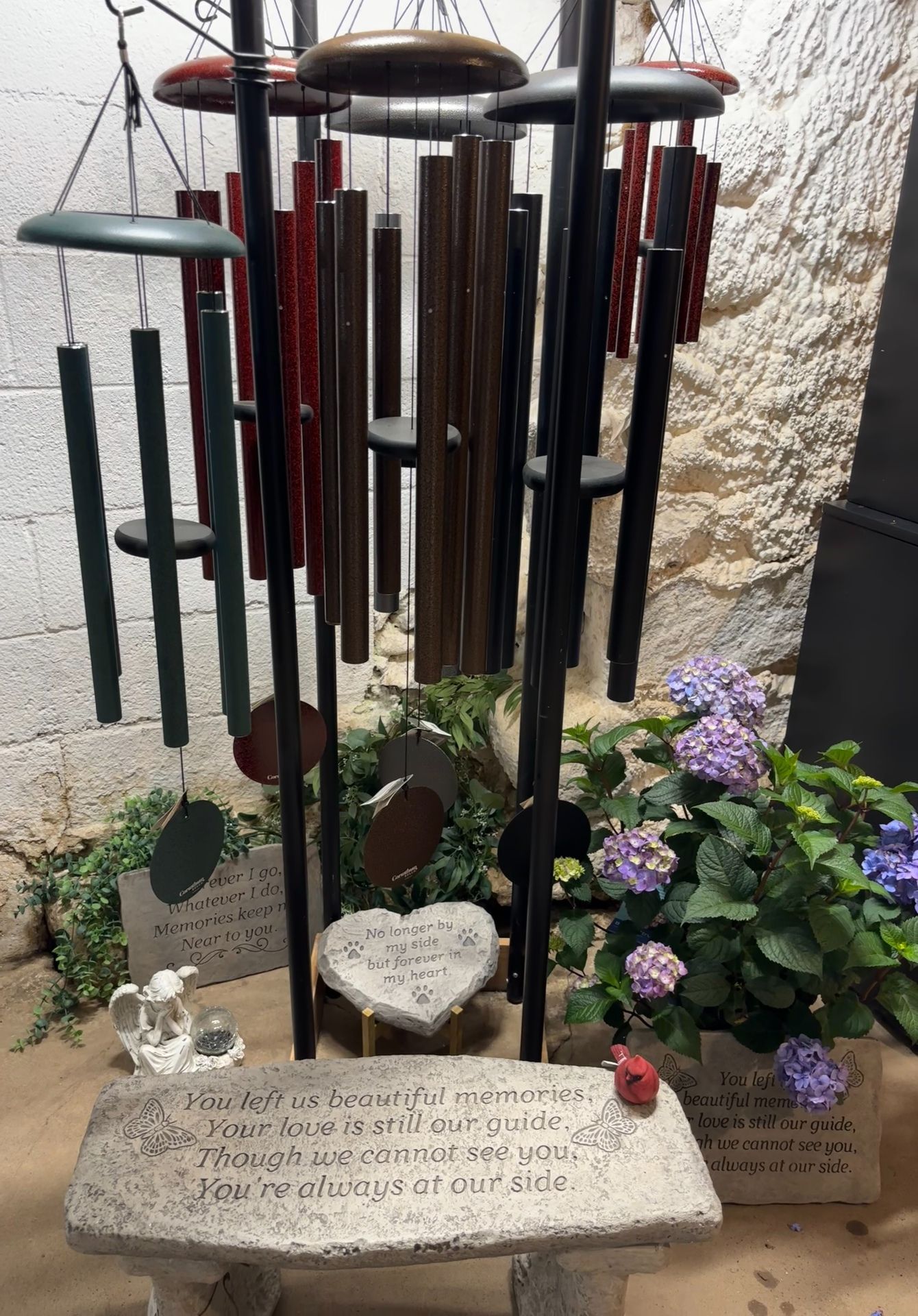Wind chimes over a garden bench with a heart-shaped stone, next to a hydrangea plant.
