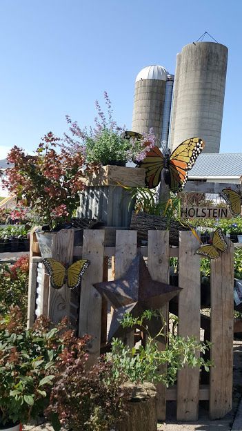 Wooden fence with metal butterflies and star, plants, and two silos in background.