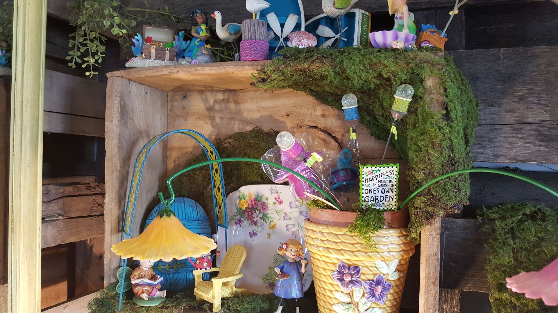 Fairy garden display in a wooden crate, featuring miniature figures, decorations, and moss.