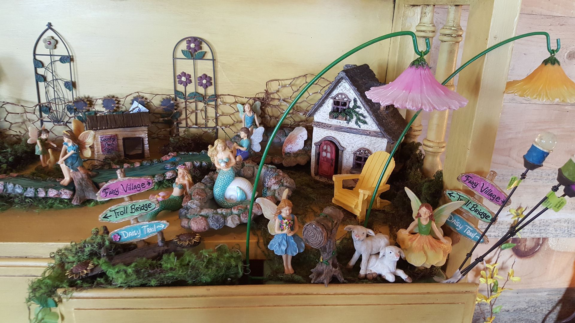 A fairy garden scene with miniature houses, fairies, and decorative plants.