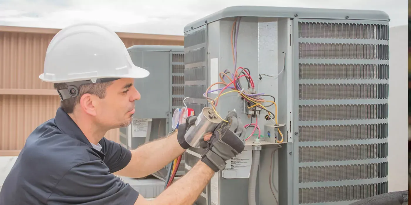 Technician in hard hat wiring an outdoor HVAC unit with tools.