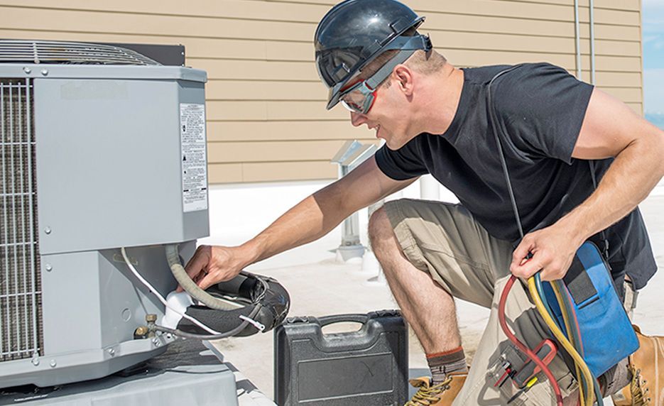 Technician kneels beside an outdoor HVAC unit, checking wires with tools in hand.