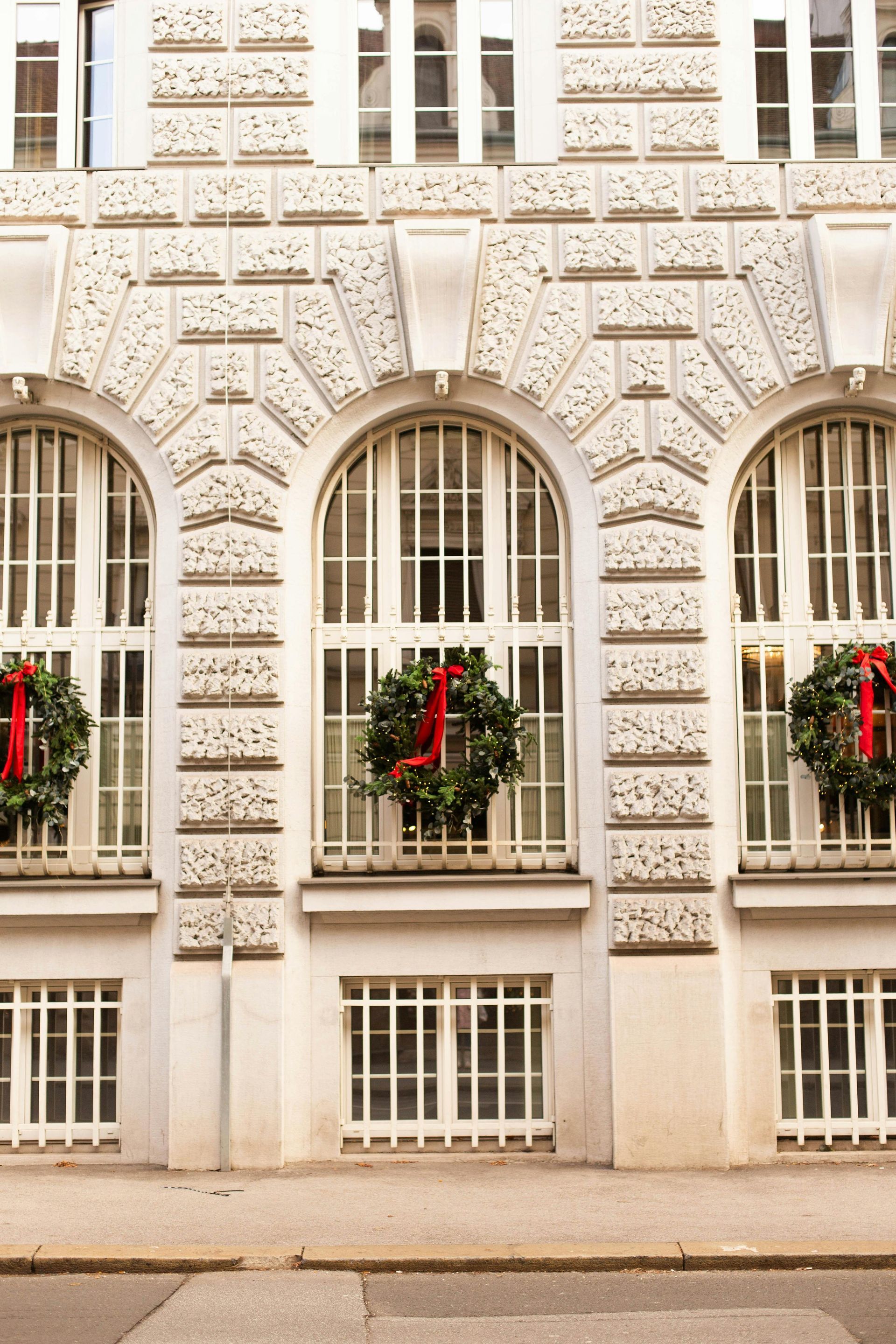 Ornate cream building facade with arched windows and red holiday wreaths on the windows