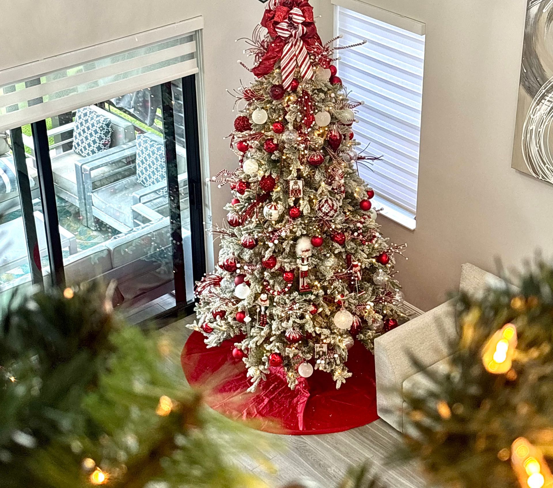 Decorated Christmas tree with red and gold ornaments in a bright living room beside windows