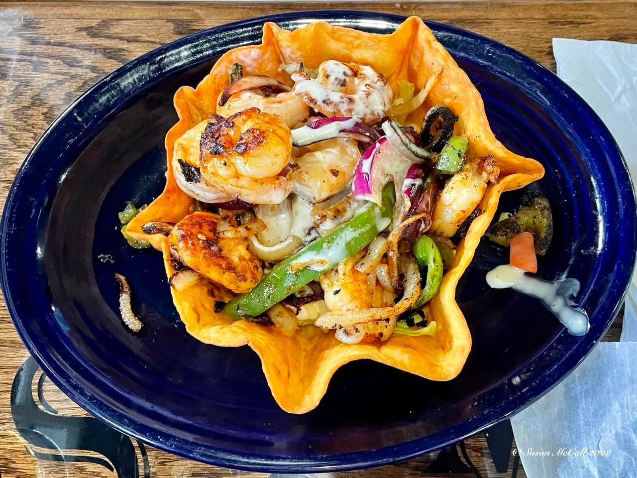 Shrimp taco salad in a crispy tortilla bowl, blue plate.