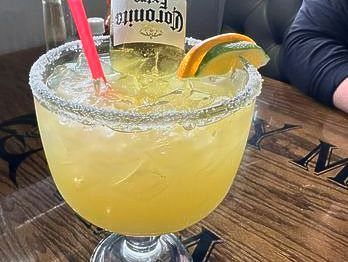 Margarita in a large glass with salt rim, Corona bottle upside down, orange slice, and straw.