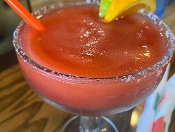Strawberry margarita in a glass with a salt rim, orange slice, lime, and straw.