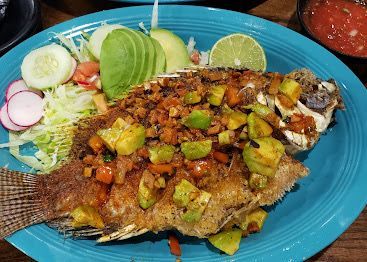 Fried fish with avocado topping, lime, and salad on a blue plate.