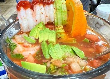 Shrimp cocktail in a large glass with avocado, tomato, orange, and cucumber garnish.
