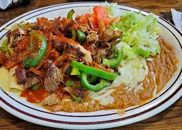Plate of Mexican food: chicken, peppers, beans, cheese, guacamole, lettuce, tomato.