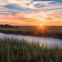 Sunset over a marsh with tall green grass, a river, and a colorful sky.