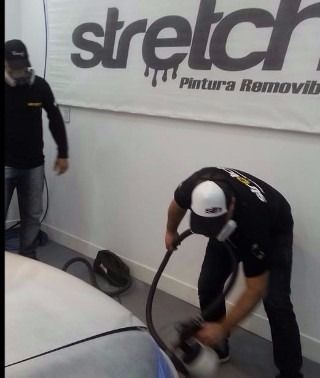 Dos trabajadores con uniformes negros utilizan una manguera para pintar una pared blanca debajo de un letrero que indica 
