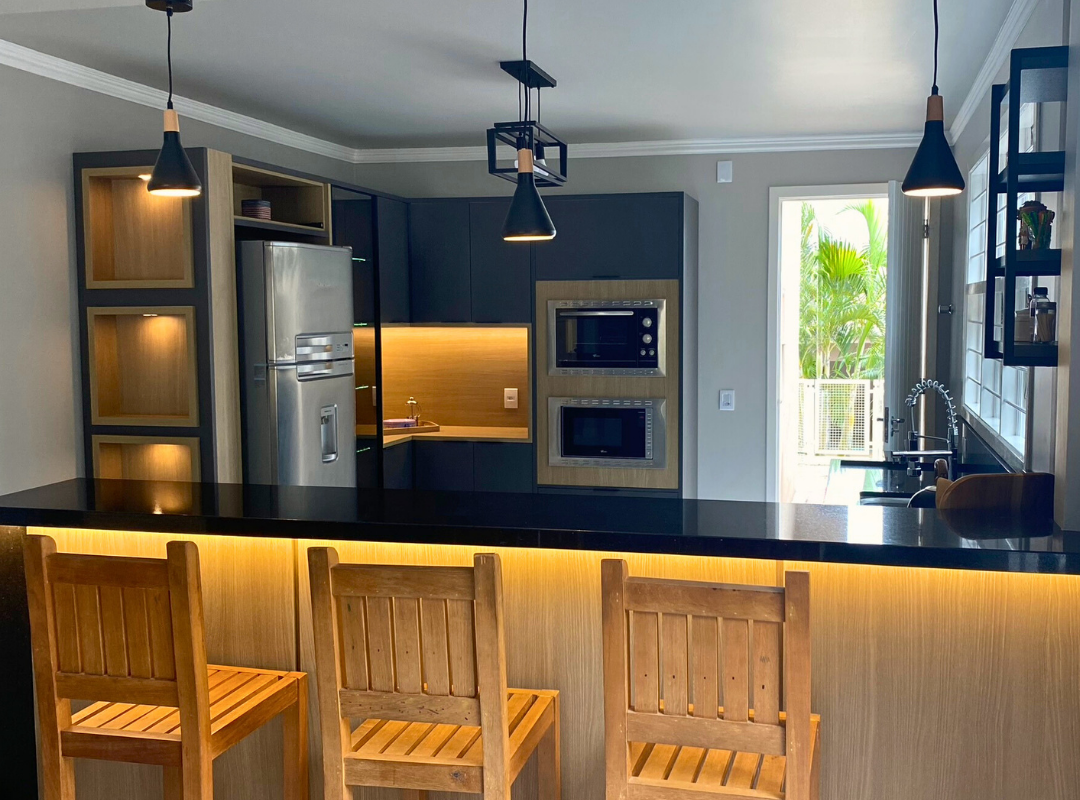 Uma cozinha com geladeira, microondas, fogão, pia e cadeiras.