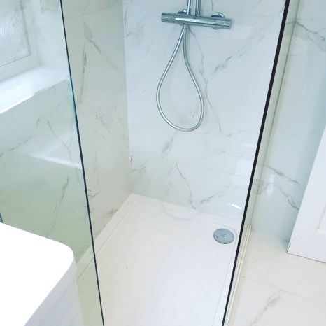 A bathroom with a walk in shower and a sink. Tiled in white marble in North West London.