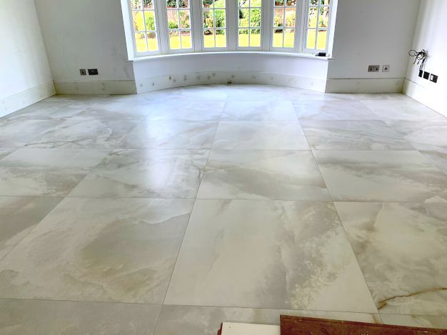 An expansive, open hall room of a luxurious London mansion. The floor is expertly tiled in soft grey marble by Master Tiling.