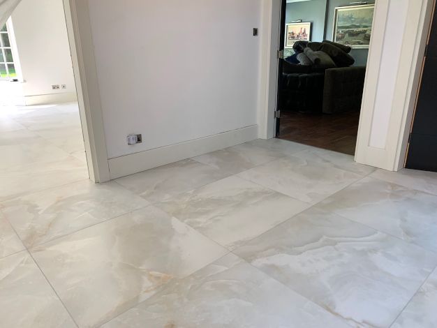 An expansive, open hall room of a luxurious London mansion. The floor is in the process of being expertly tiled in soft grey marble by Master Tiling.