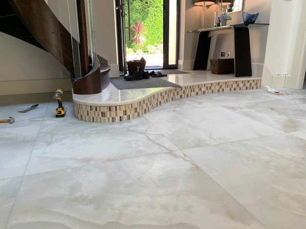 An expansive, open hall room of a luxurious London mansion. The floor is expertly tiled in soft grey marble by Master Tiling.