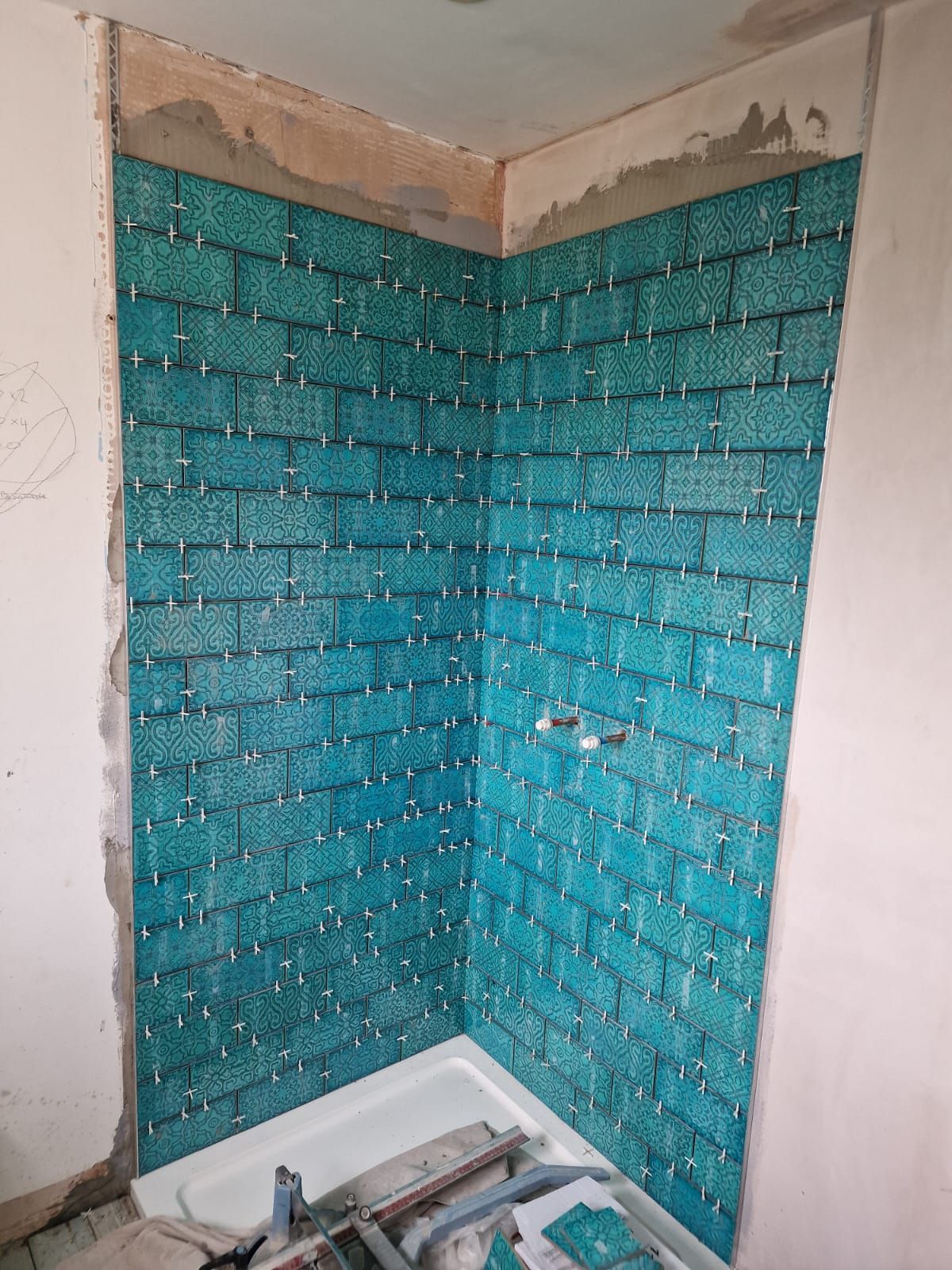 A bathroom tiling project underway in London. The blue metro tiles are carefully lined up and being grouted to create the shower walls. 