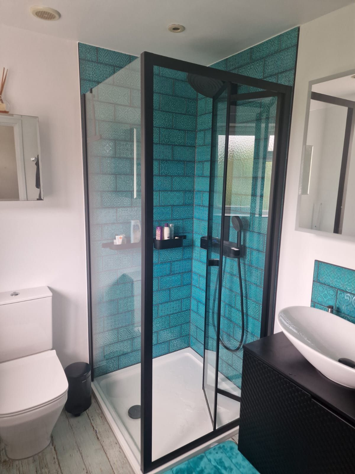 A newly completed bathroom tiling installation by Master tiling, the tiles are light turquoise blue metro tiles and the shower is fitted with black details.