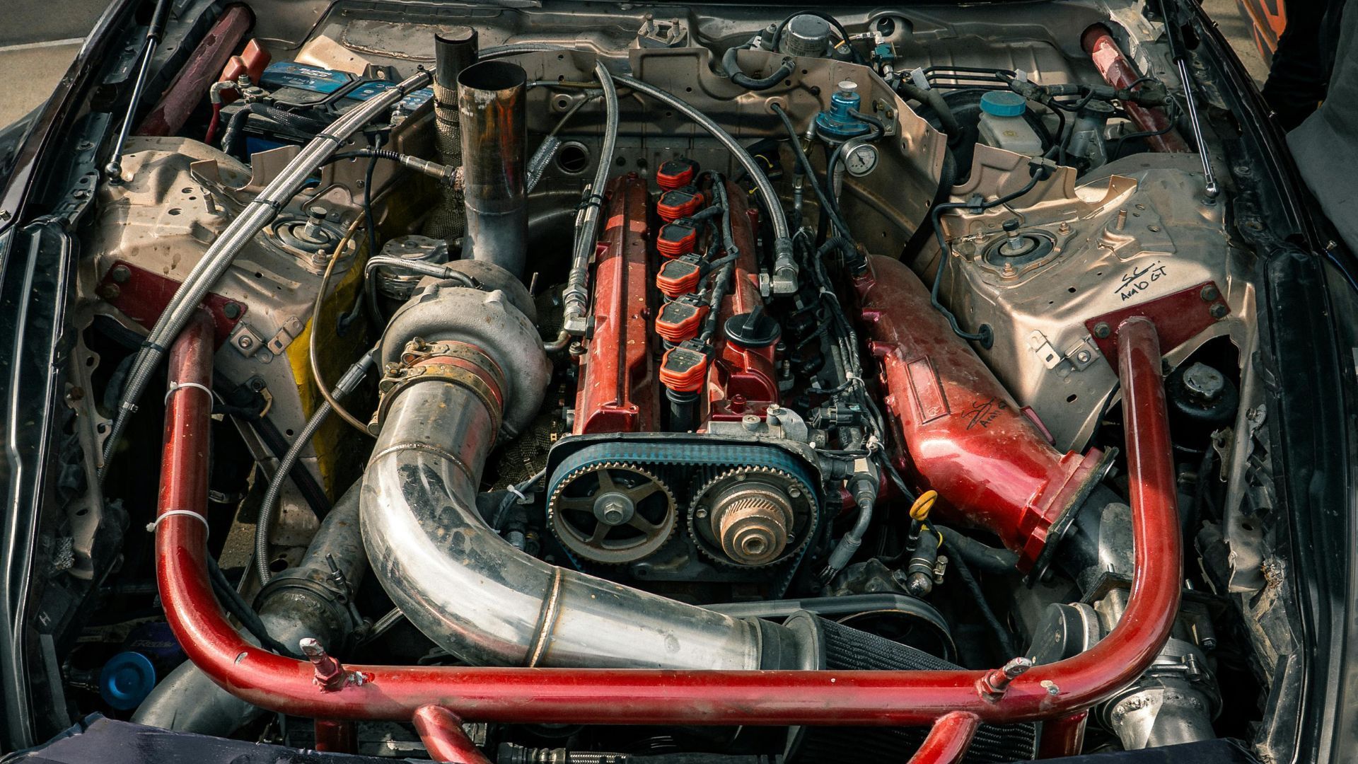 High-angle view of a customized automotive engine bay featuring a large silver turbocharger and a bright red valve cover.