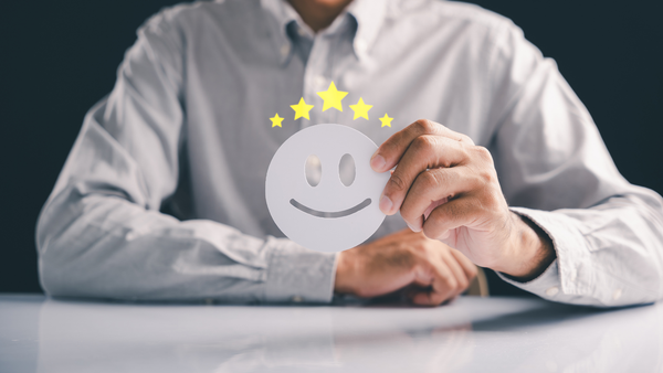 A person holds a white paper cutout of a smiling face with five yellow stars above it.
