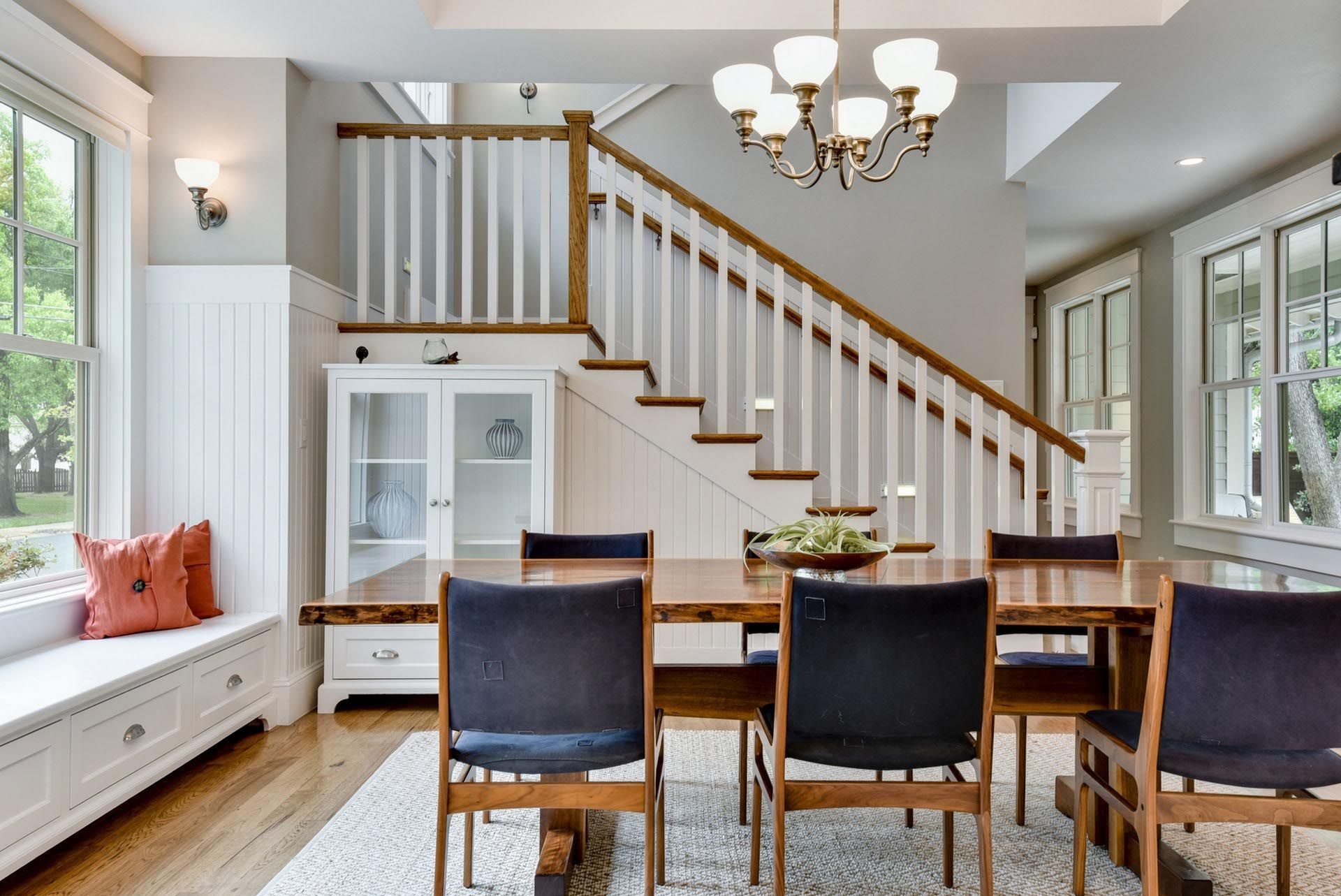 Dining room with wooden table and chairs, staircase, window seat, and chandelier.