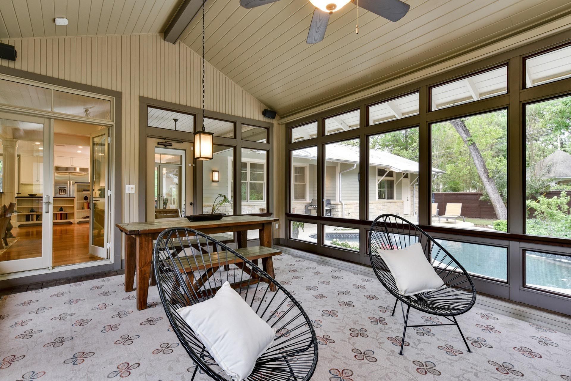 Sunroom with dark-framed windows, two black chairs with white cushions, and a wooden table.