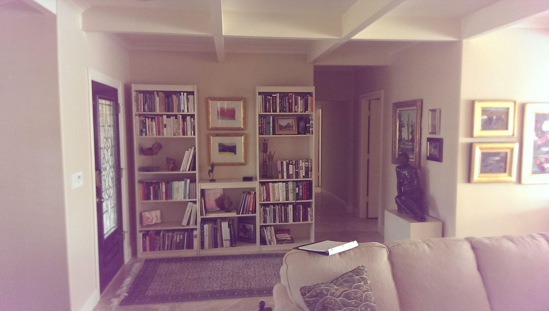 Living room with bookshelves, art, and a couch. Entrance door on the left, hallway on the right.