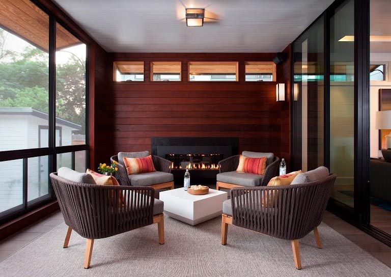 Cozy outdoor living area with fireplace, four chairs, square coffee table, and large windows.