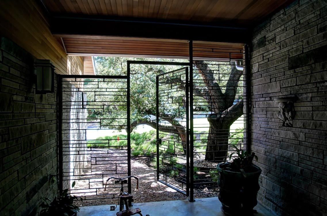 Interior view through a decorative iron gate, framing a tree in an outdoor garden.
