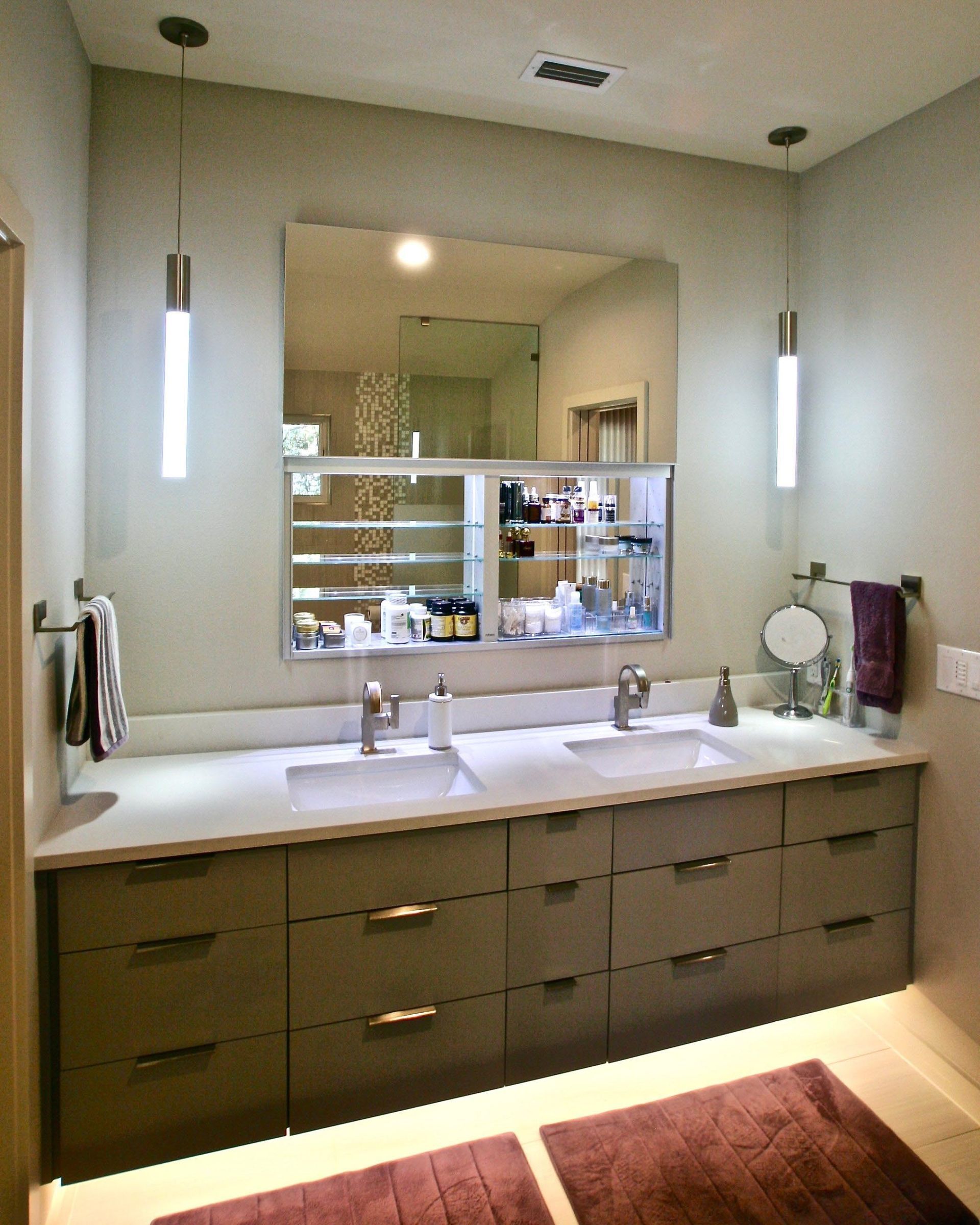 Modern bathroom with dual sinks, large mirror, and gray cabinetry. Two vertical lights flank the mirror.
